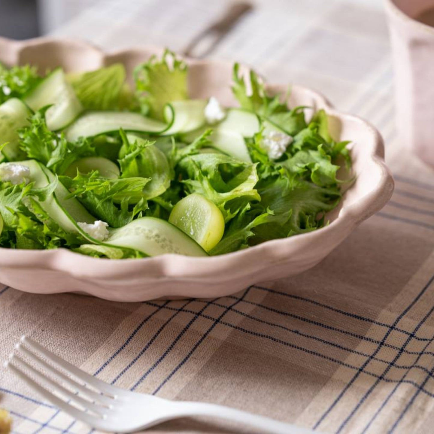 Bowl of green salad on a checkered tablecloth with a fork and cup in the background.