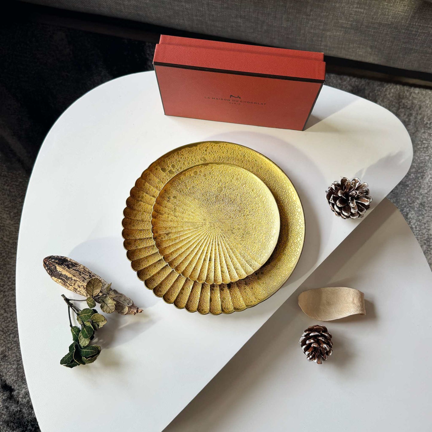 Decorative plates with a red box and natural elements on a white surface