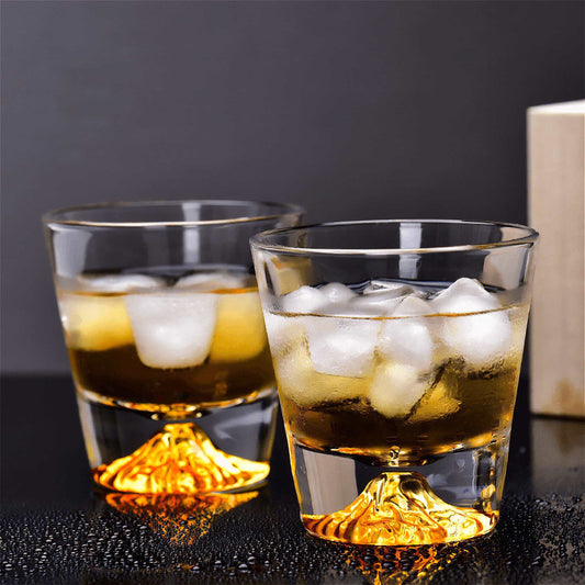 Two glasses of whiskey with ice cubes on a dark surface