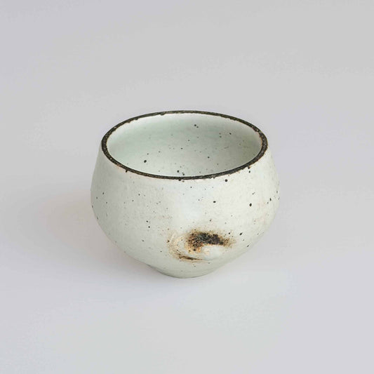 A small, white, speckled ceramic cup with a dark brown rim, set against a plain white background.