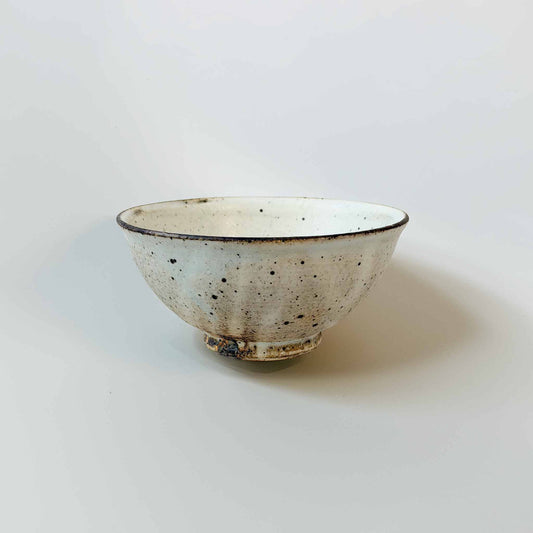 A small, handcrafted white ceramic bowl with a V-shaped design and kohi glaze, set against a plain white background.