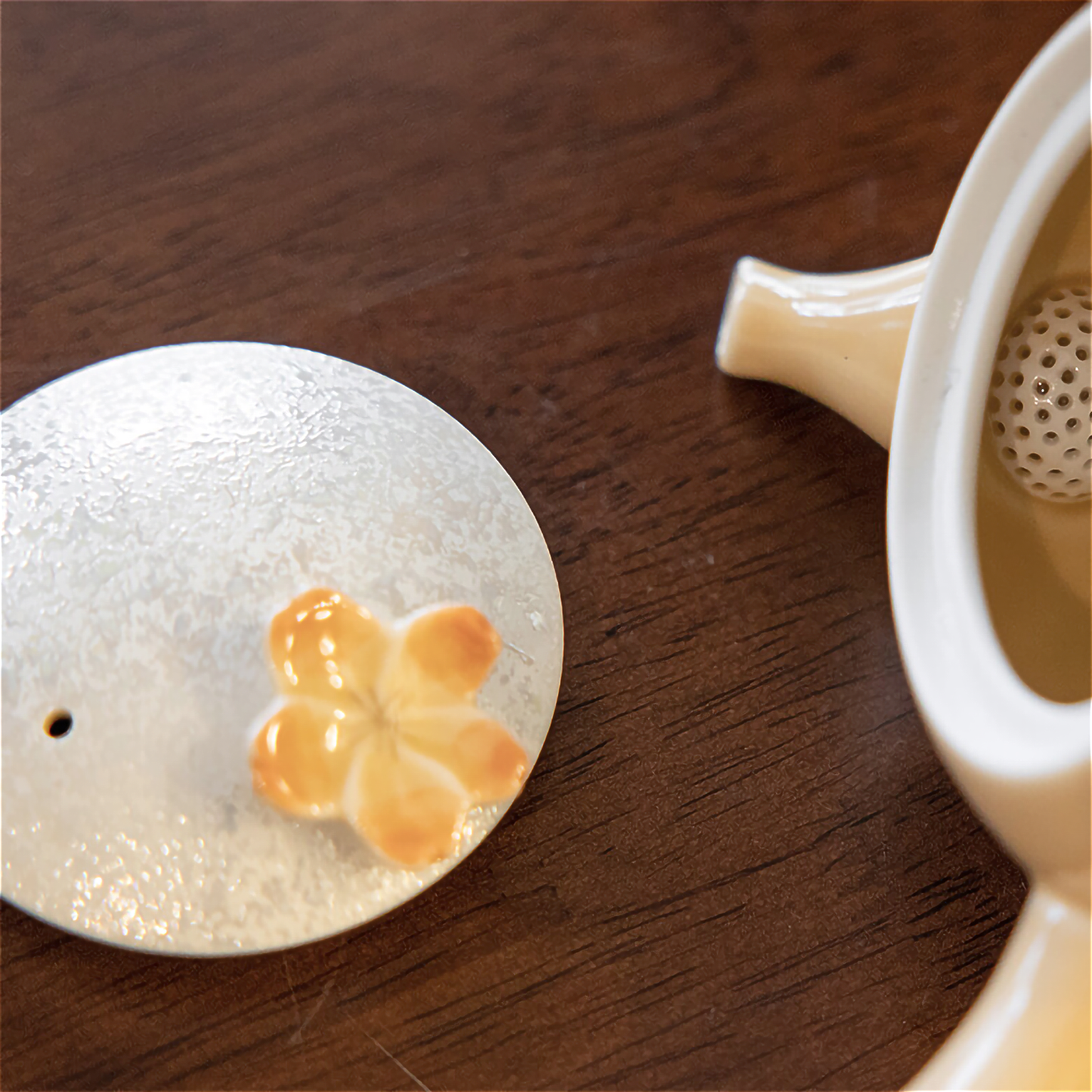 Tea infuser with floral design on a wooden surface next to a teacup.
