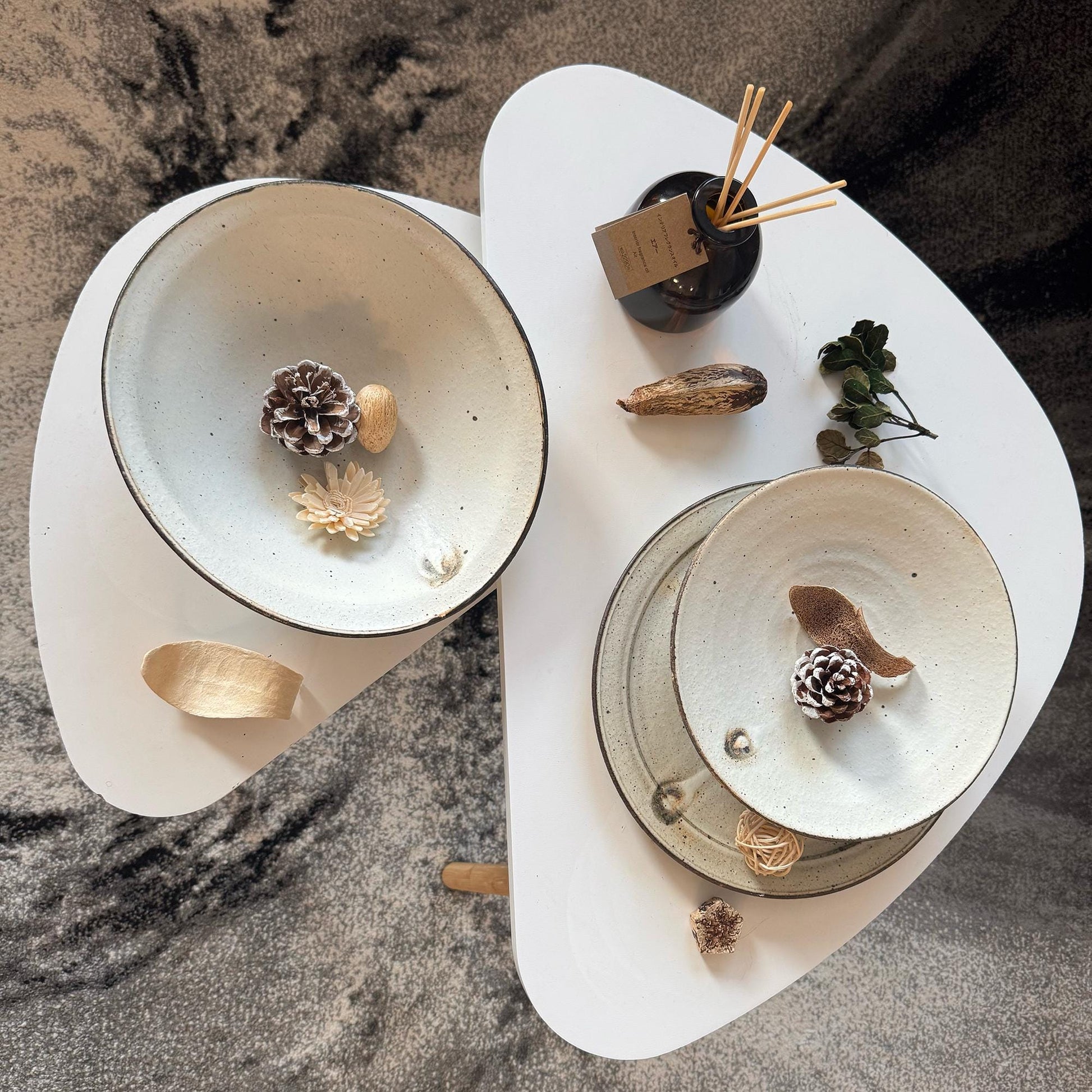 Two handcrafted, shallow, white ceramic bowls with a subtle, speckled glaze, created by Japanese artisan Takashi Sogo.