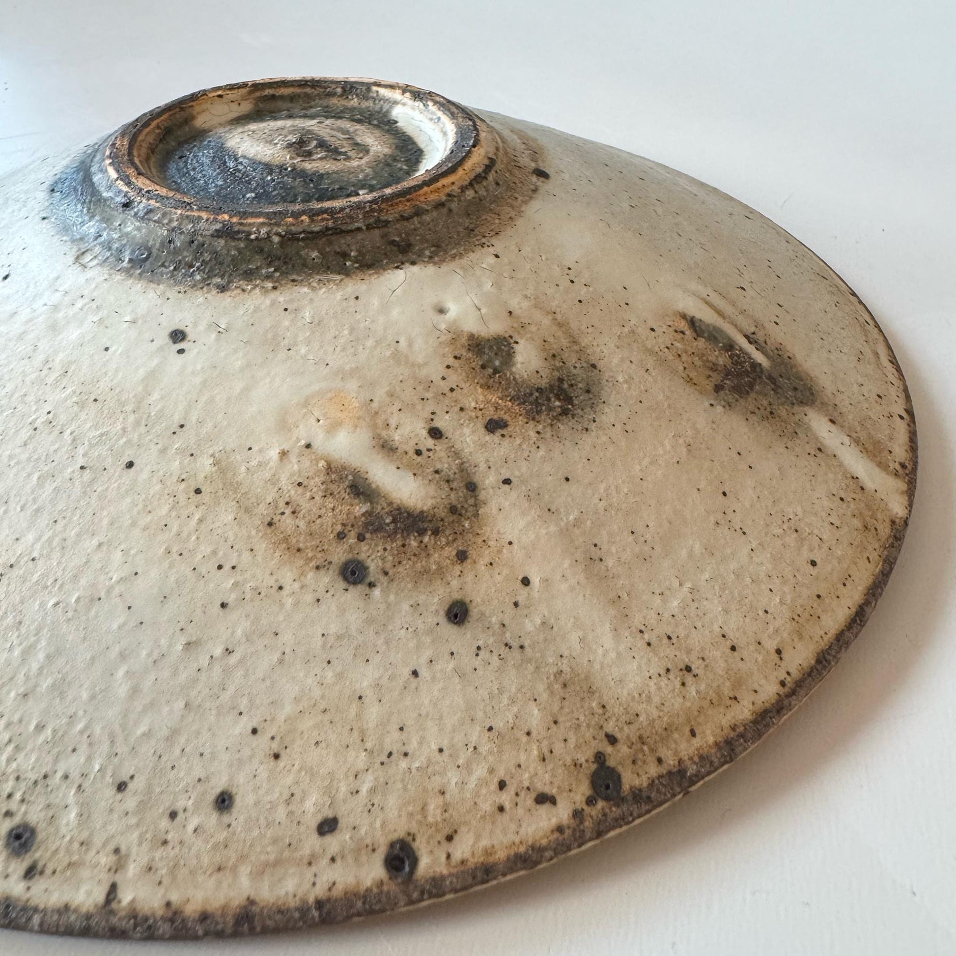 A handcrafted, shallow ceramic bowl with a subtle, earthy tone and a speckled glaze, evoking a sense of understated beauty.