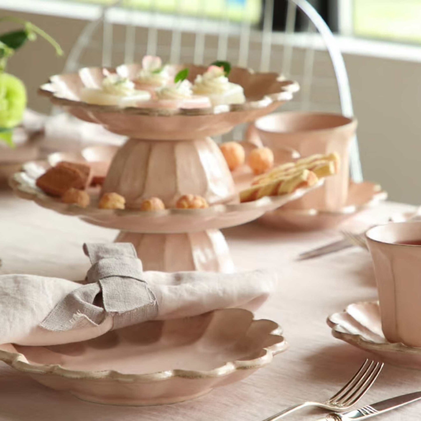 Tea party setup with pastel pink teacups, plates, and a cake stand.