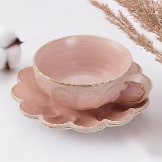 Pink ceramic cup and saucer with gold accents on a white background