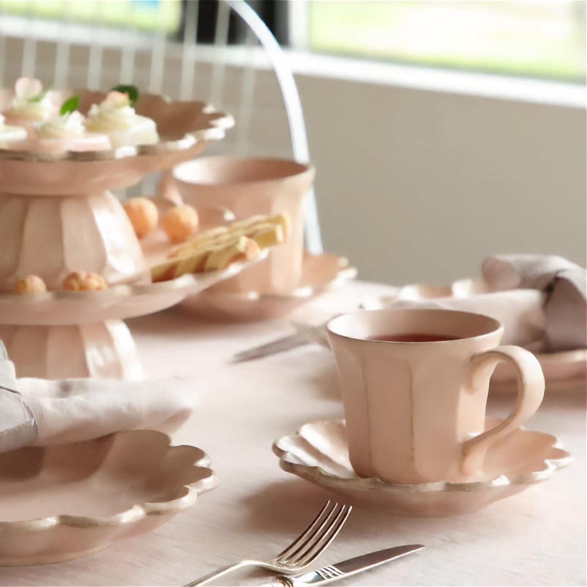 Dessert table setting with pastel pink plates, cups, and a tiered stand.
