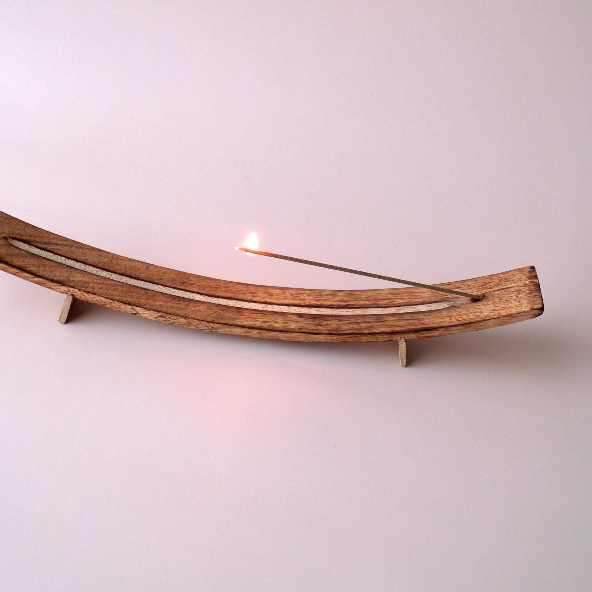 Wooden incense holder with a lit incense stick on a light pink background