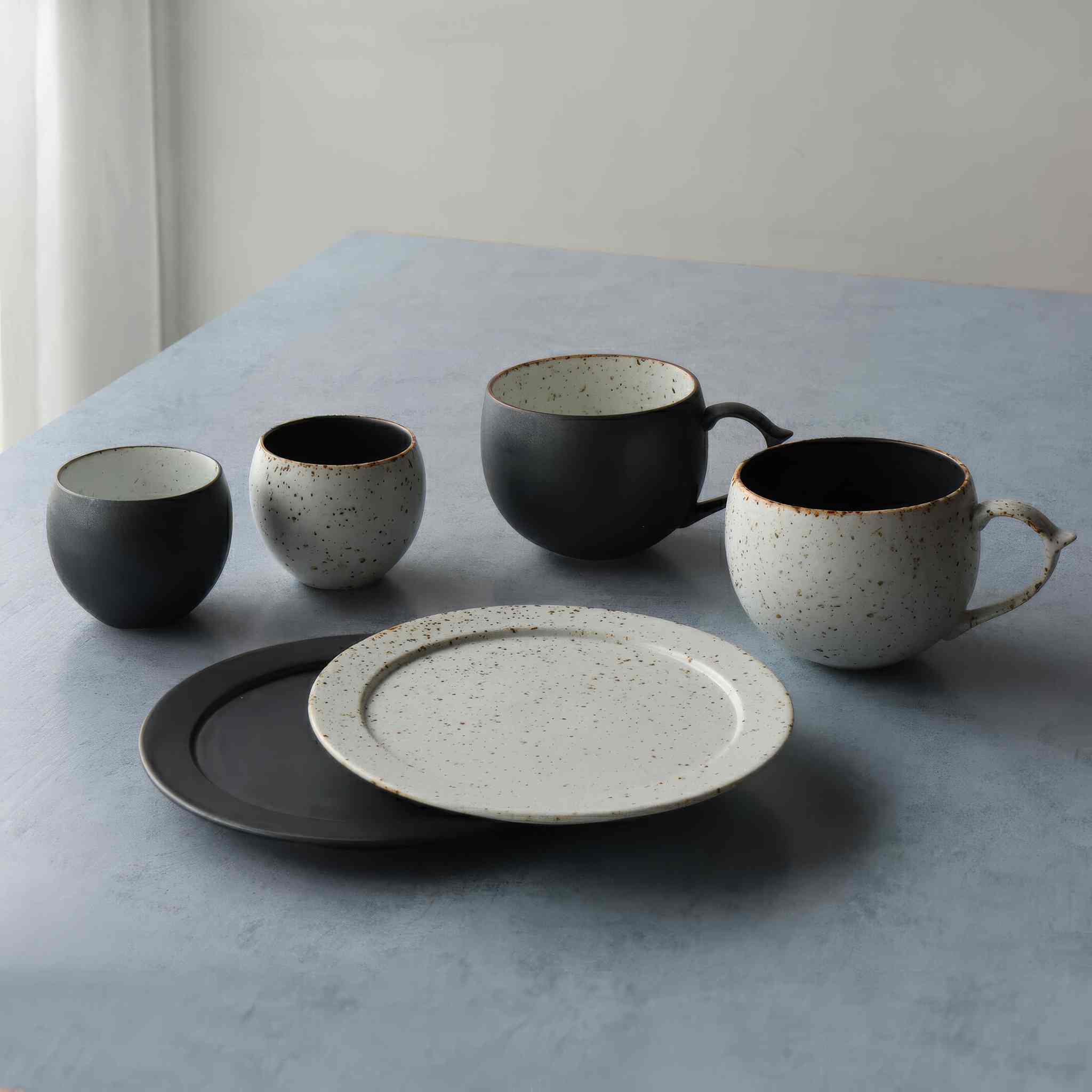 A small, handmade plate with a black and white speckled glaze, sitting on a table.