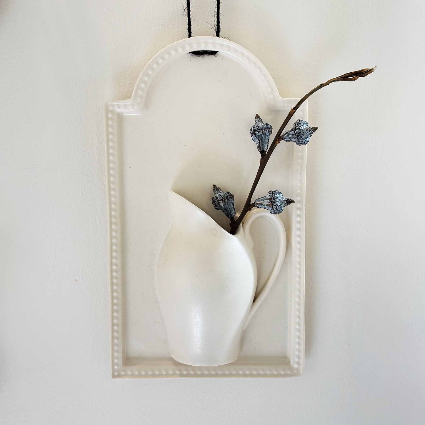 A white, hand-painted wall vase with a deep, richly-inked tau.