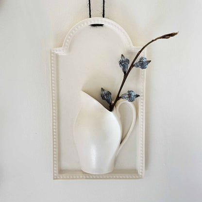 A white, hand-painted wall vase with a deep, richly-inked tau.