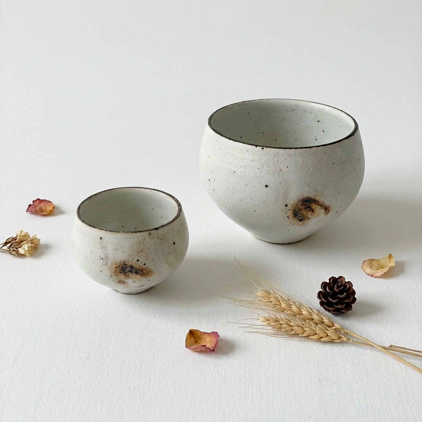 Handmade ceramic soup cup with natural glaze, placed on a white surface with dried flowers and a pinecone.