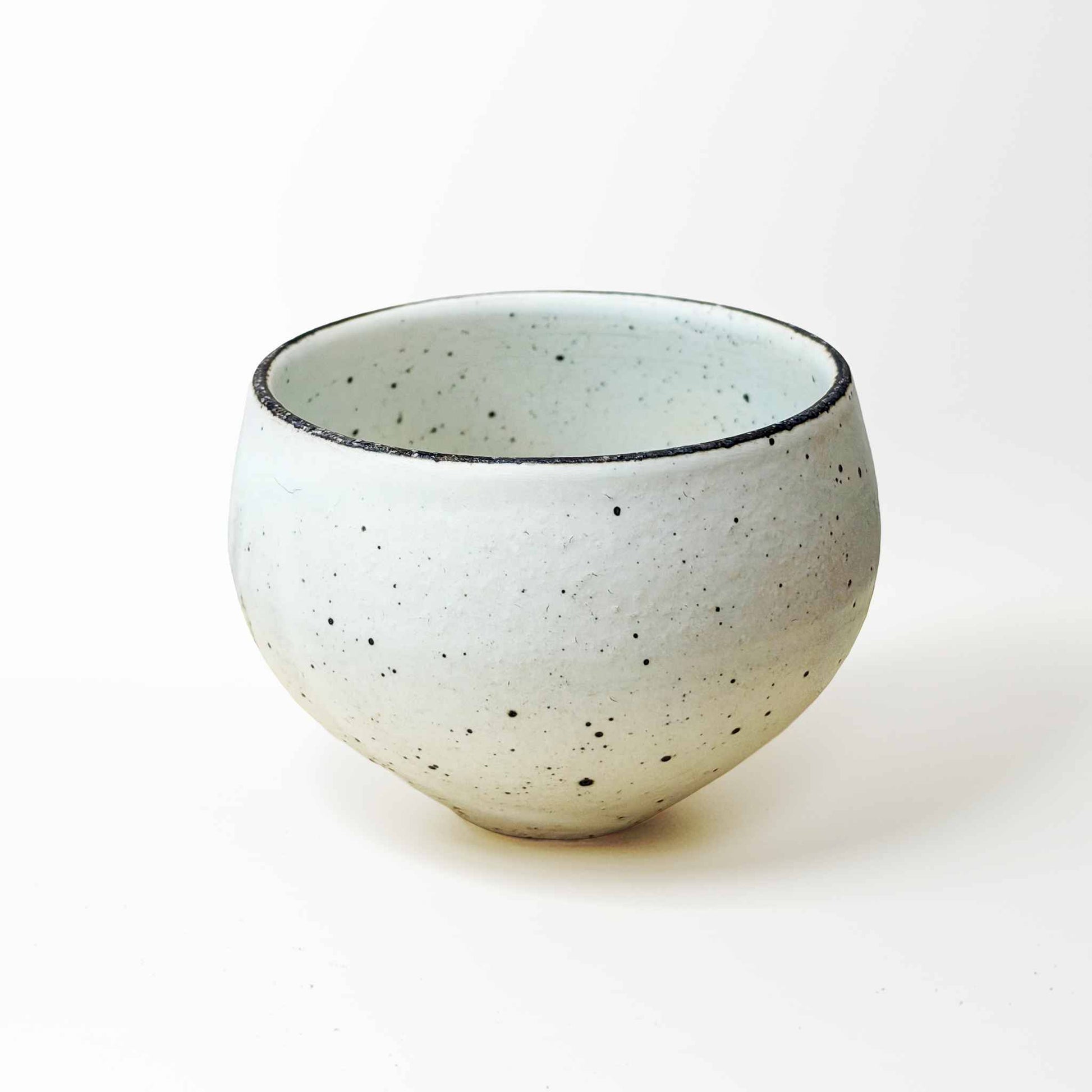 A small, white, speckled ceramic bowl with a natural glaze, set against a plain white background.