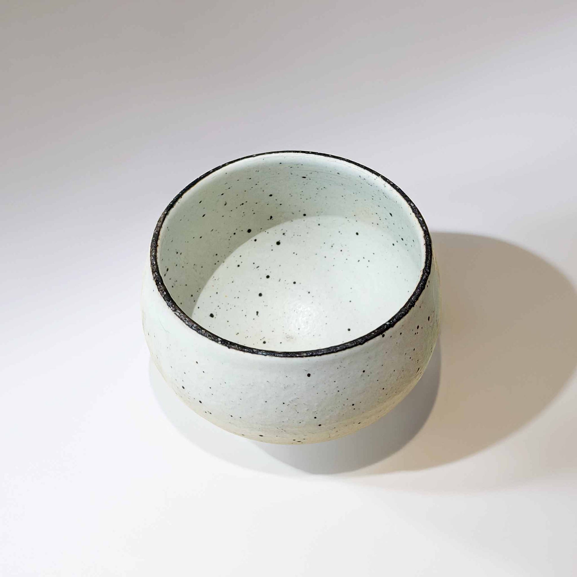 A white, speckled, handcrafted ceramic soup cup with a natural glaze, set against a neutral background.