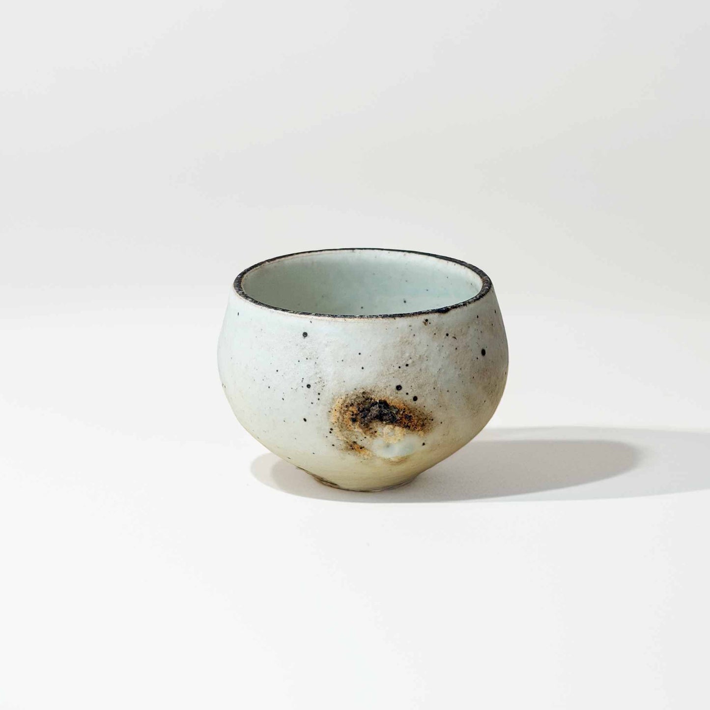 A small, handcrafted white ceramic soup cup with a natural glaze and subtle textures, set against a neutral background.