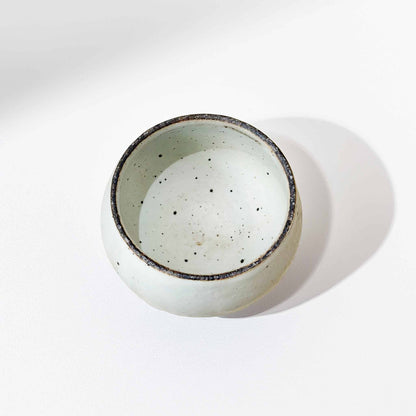 A small, white, speckled ceramic bowl with a natural glaze, set against a plain white background.