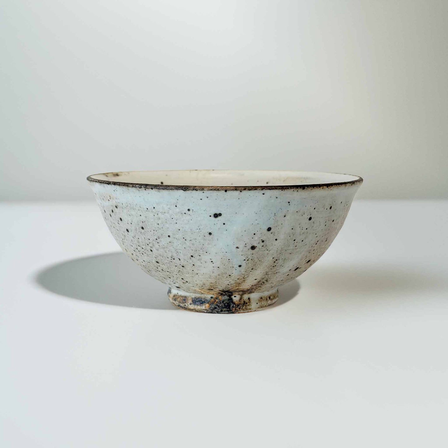 A small, handcrafted, white ceramic bowl with a kohiki glaze and V-shaped design, set against a neutral background.