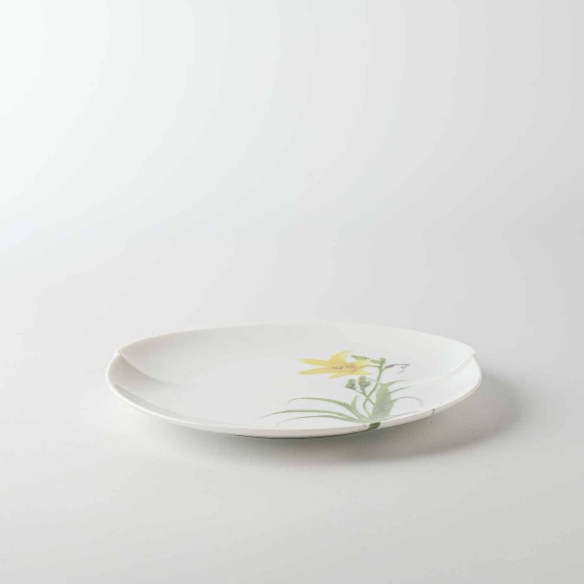 A delicate white porcelain plate with a small, yellow daisy design.