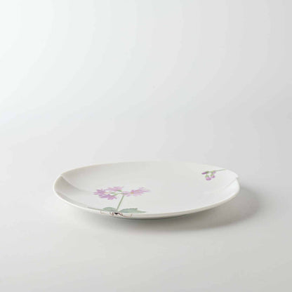 A delicate white porcelain plate with a small, vibrant daisy design in soft pink and green.
