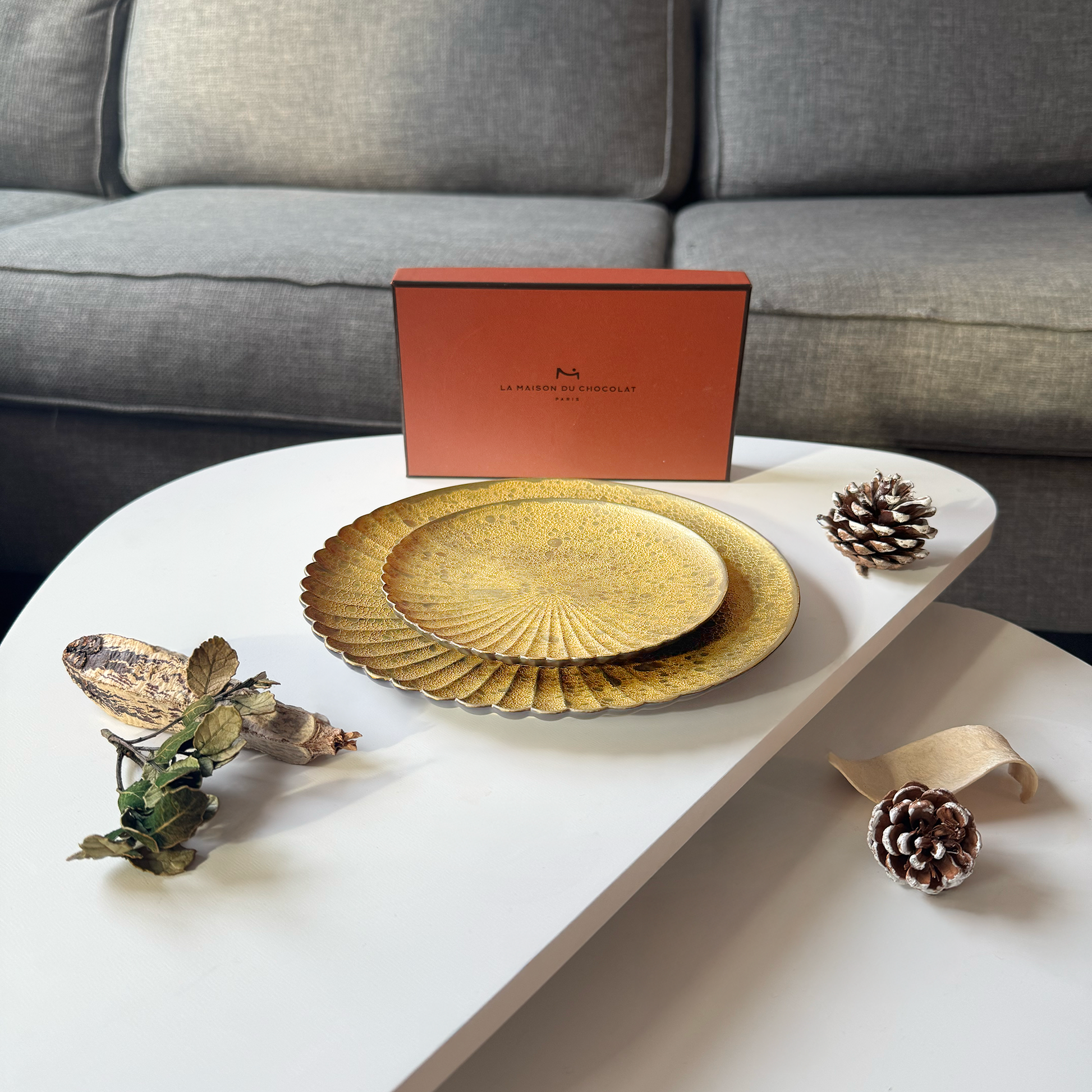 Gold decorative plates on a white table with a gray couch in the background