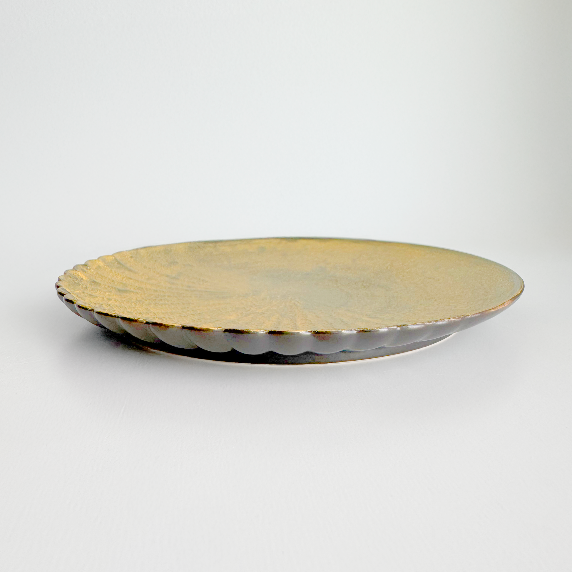 Round metallic plate with scalloped edge on a light gray background