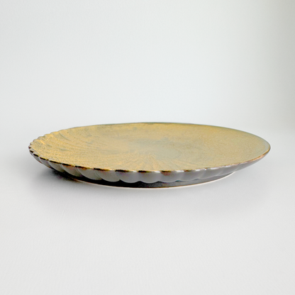 Round metallic plate with scalloped edge on a light gray background