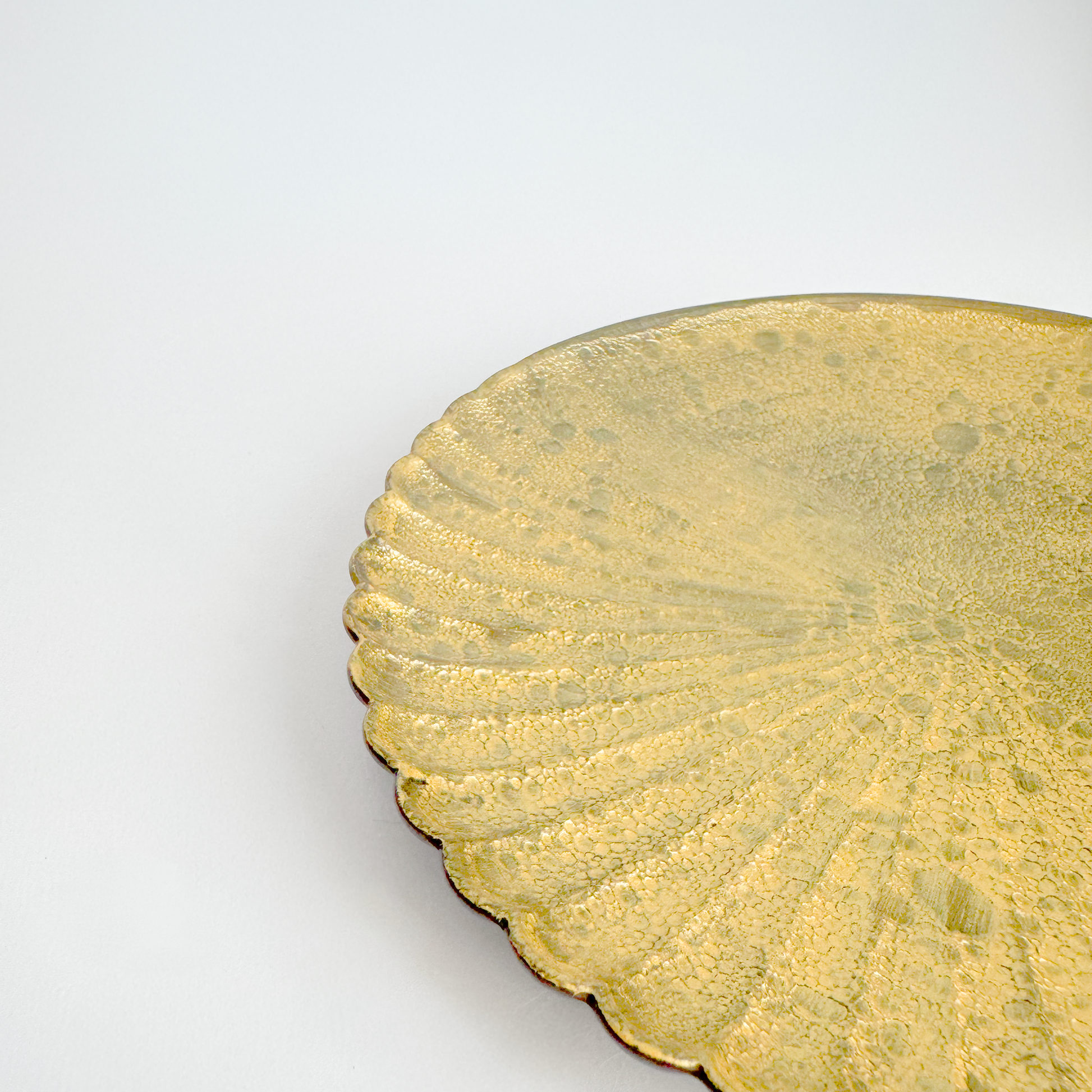 Close-up of a gold decorative plate with scalloped edge on a white background