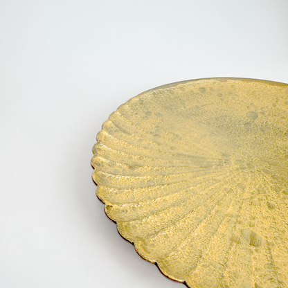 Close-up of a gold decorative plate with scalloped edge on a white background