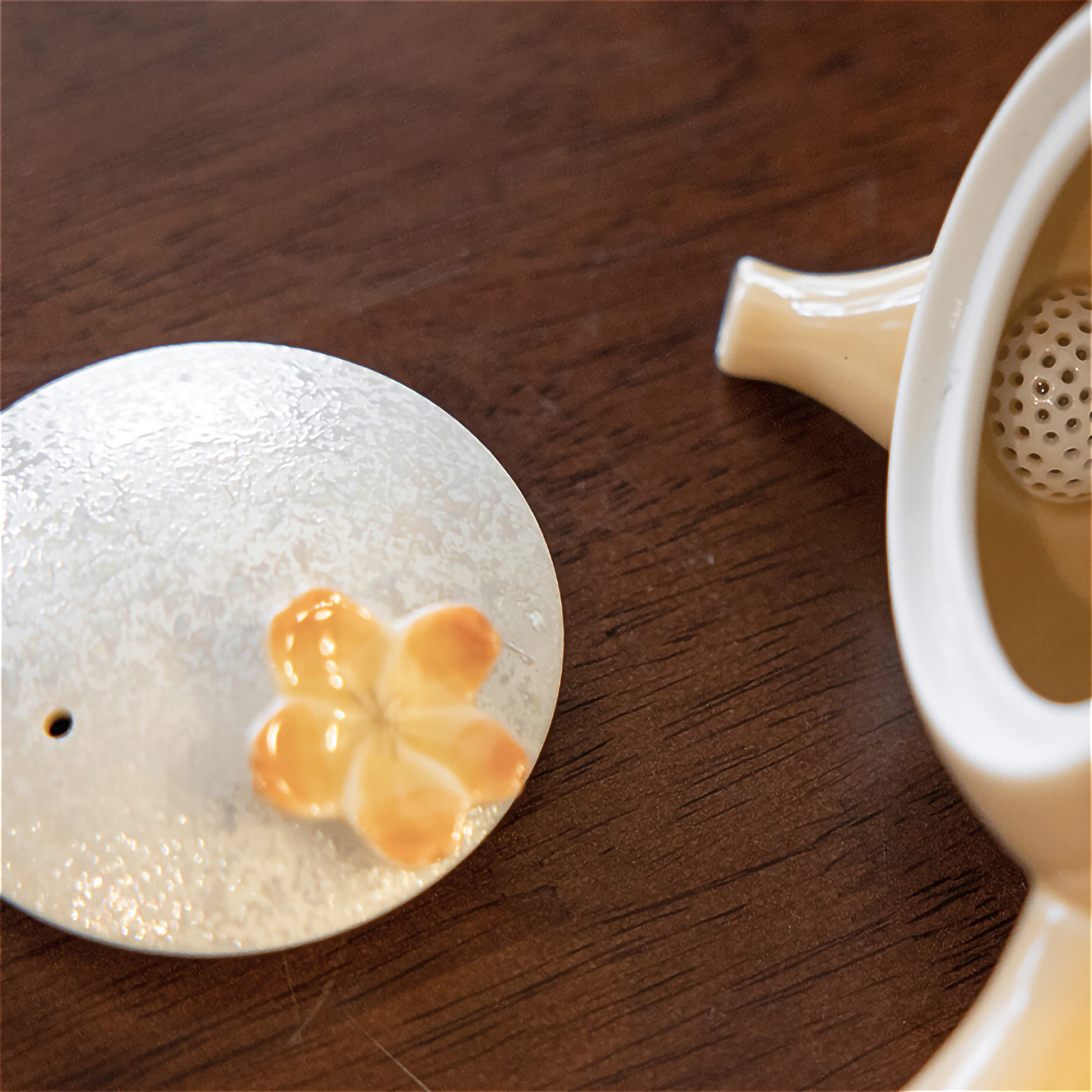 Tea infuser with floral design on a wooden surface next to a teacup.