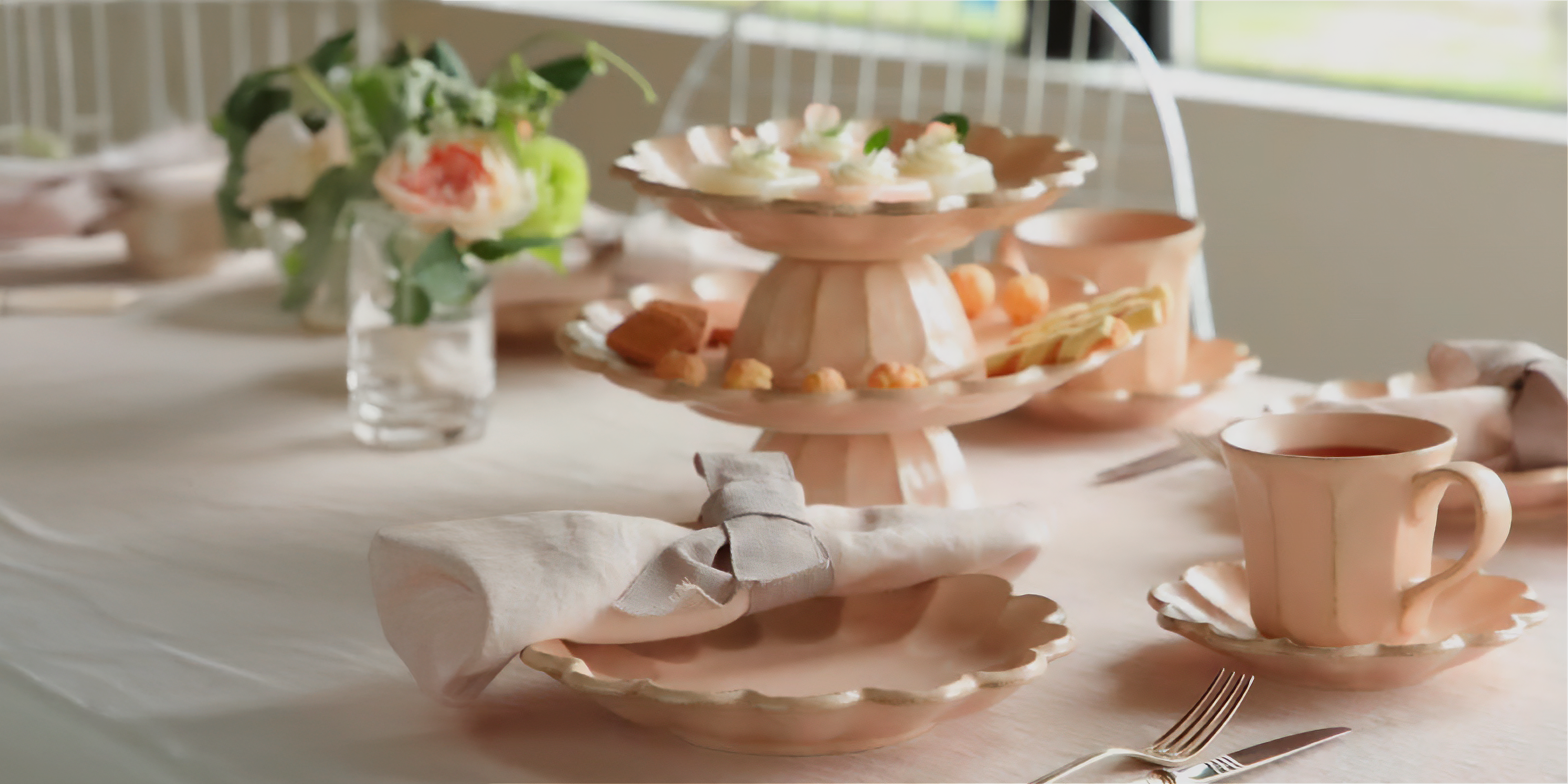 Tea set with cups, saucers, and pastries on a table with a floral arrangement.